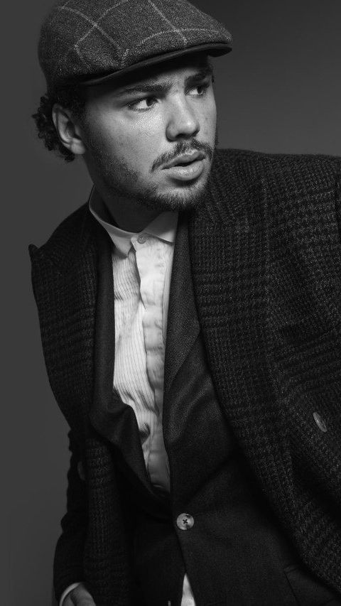 Man in tweedjas en pet, kijkt opzij, draagt ​​een overhemd met kraag.