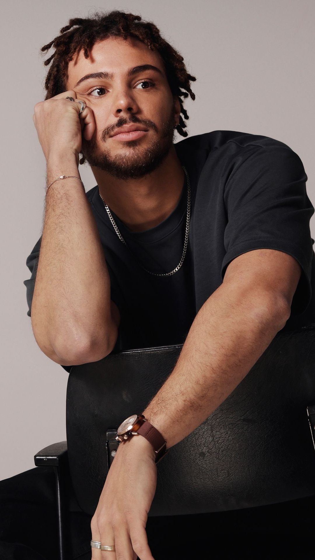 Man met dreadlocks, die zijn kin op zijn hand laat rusten, gekleed in een donker shirt en met een horloge.