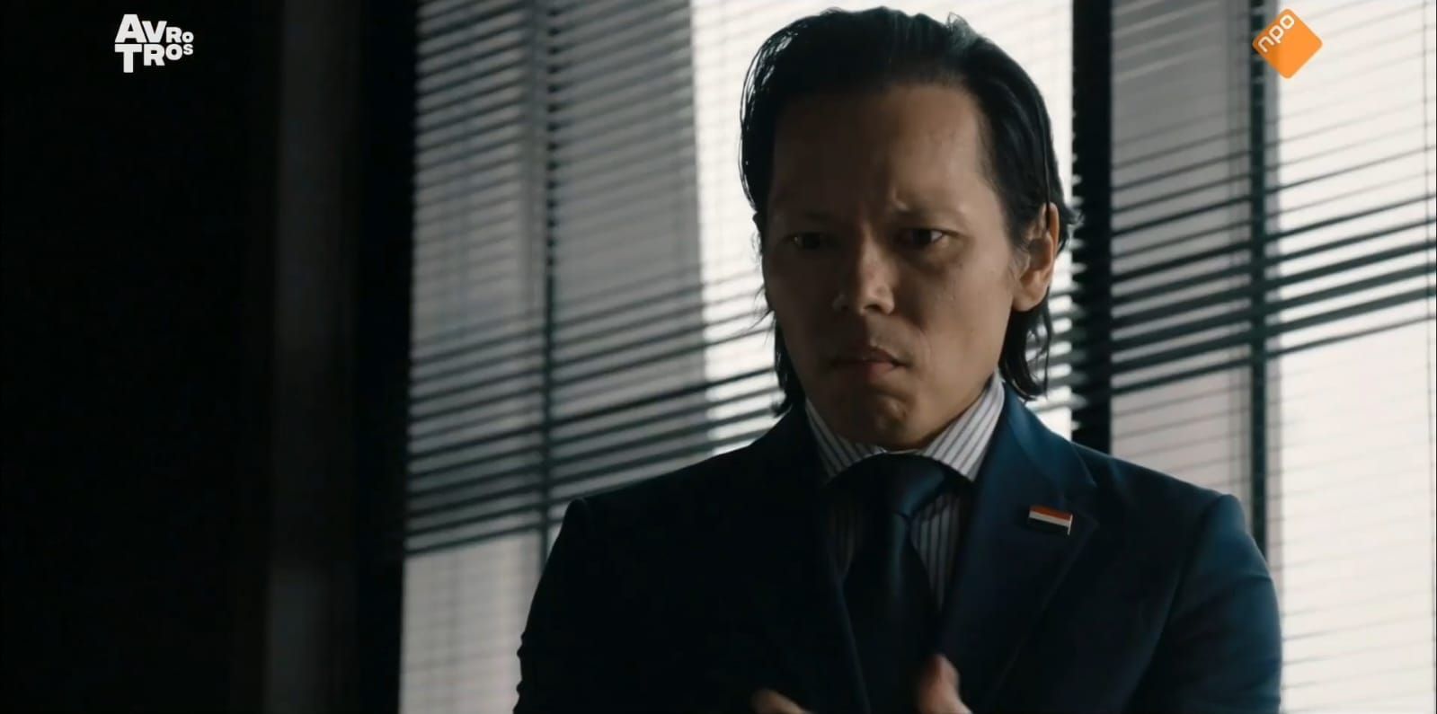 Een man in pak staat bezorgd voor een raam.