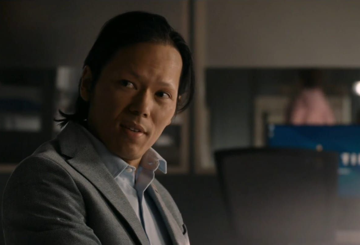 Man in grijze blazer, kijkt iets opzij, in een kantooromgeving.