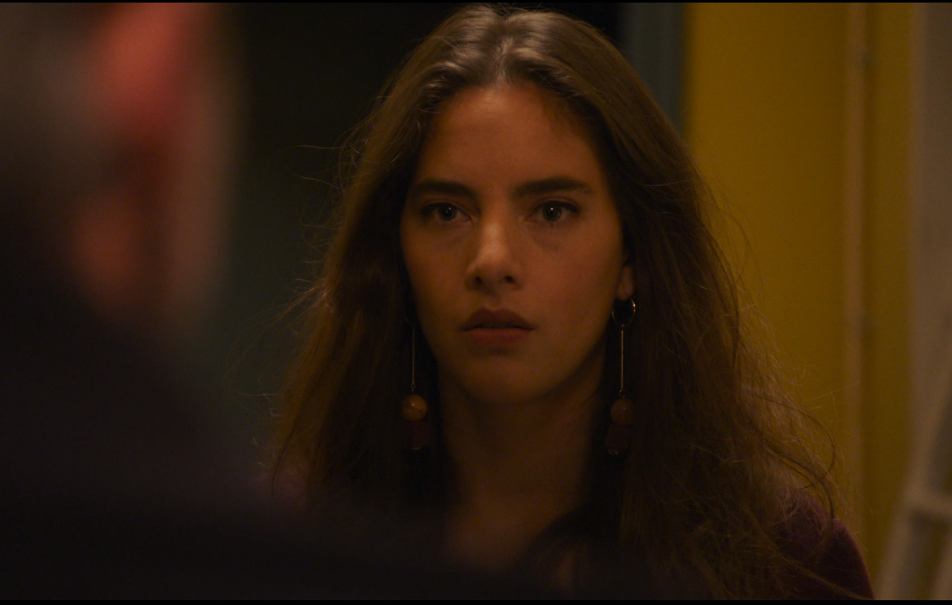 Een vrouw met lang bruin haar en oorbellen kijkt met een bezorgde blik naar iemand buiten beeld.