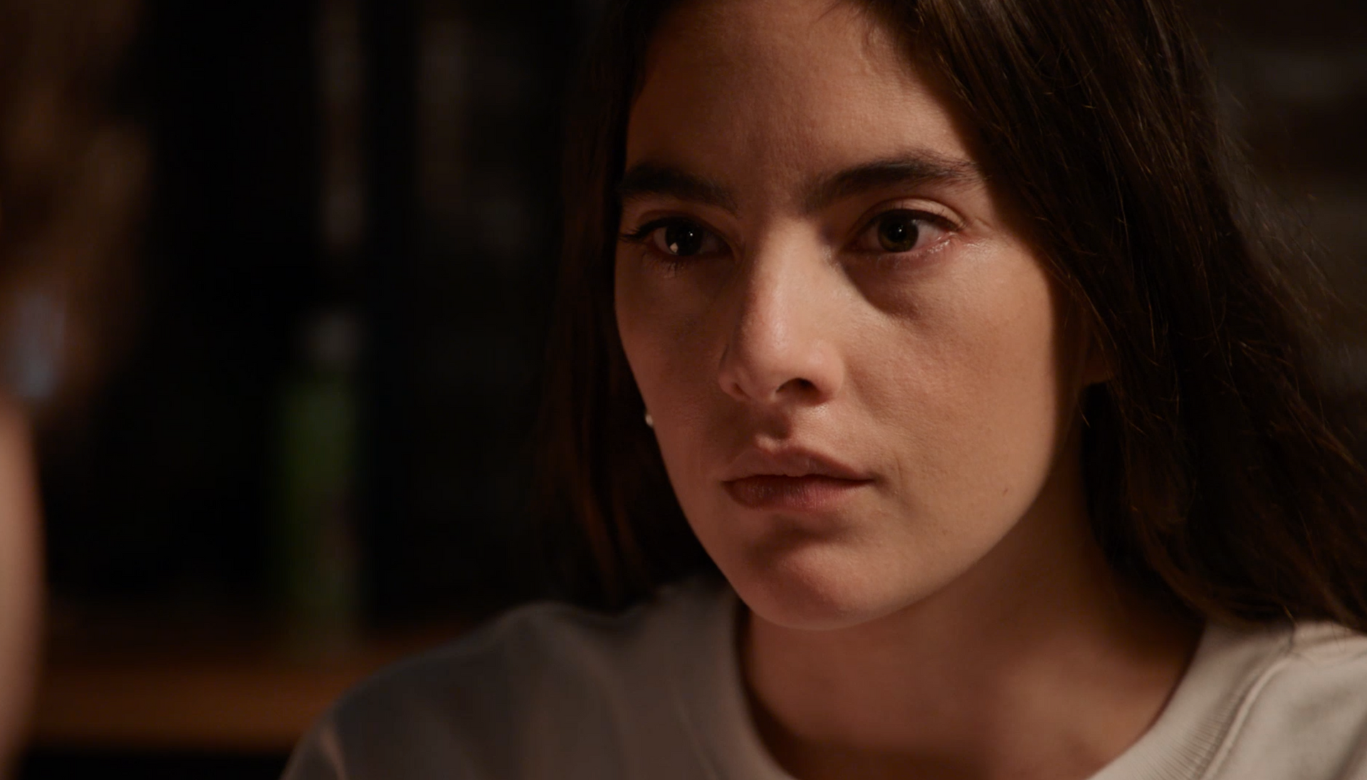 Vrouw met bruin haar, ernstige uitdrukking, kijkt naar beneden. Close-up in gedempt licht.