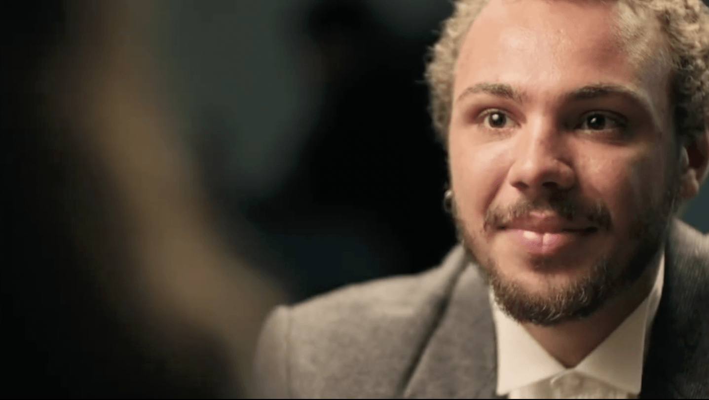 Man met blond krullend haar en een baard, gekleed in een pak, glimlachend en iets naar rechts kijkend.