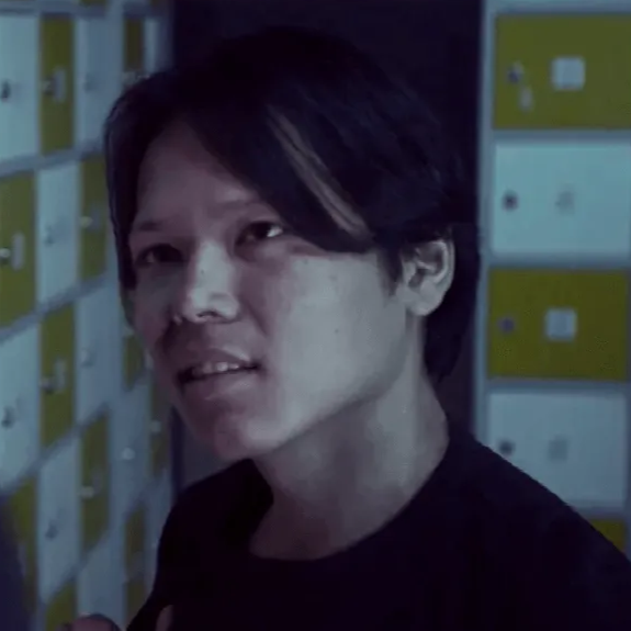 Een persoon spreekt iemand aan in een kleedkamer. Deze persoon heeft donker haar en draagt een zwart shirt.