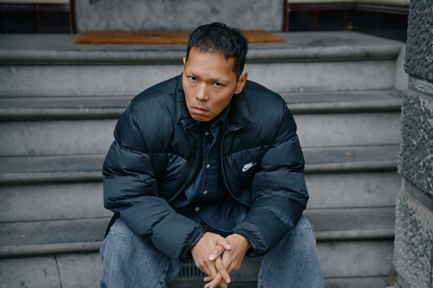 Een man in een blauwe gewatteerde jas zit bezorgd op een buitentrap.