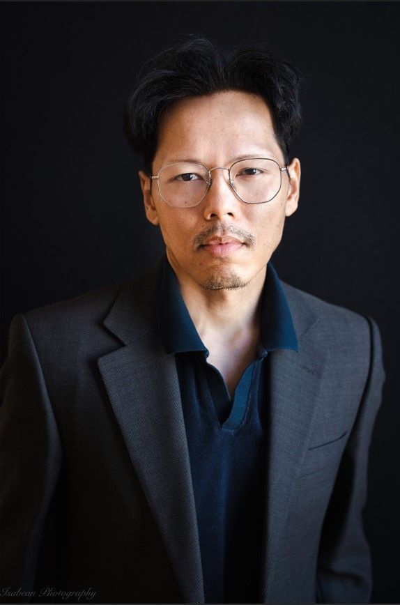 Man met bril en colbert, donkere achtergrond.