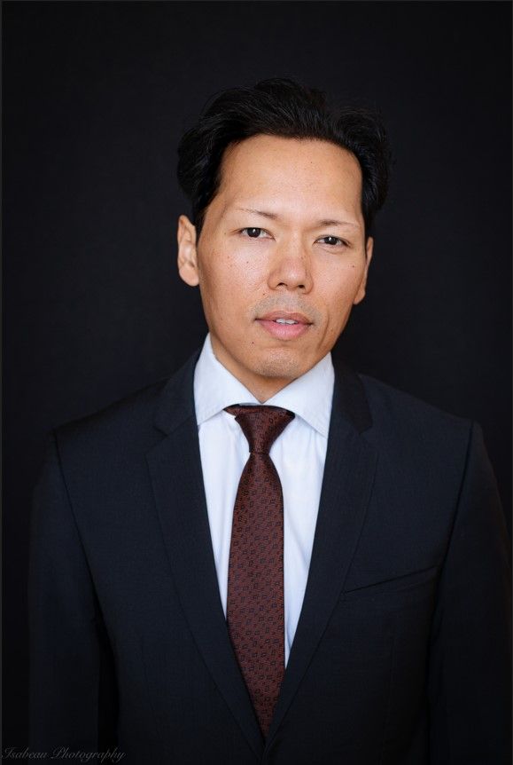 Man in een donker pak met een bordeauxrode stropdas tegen een zwarte achtergrond.