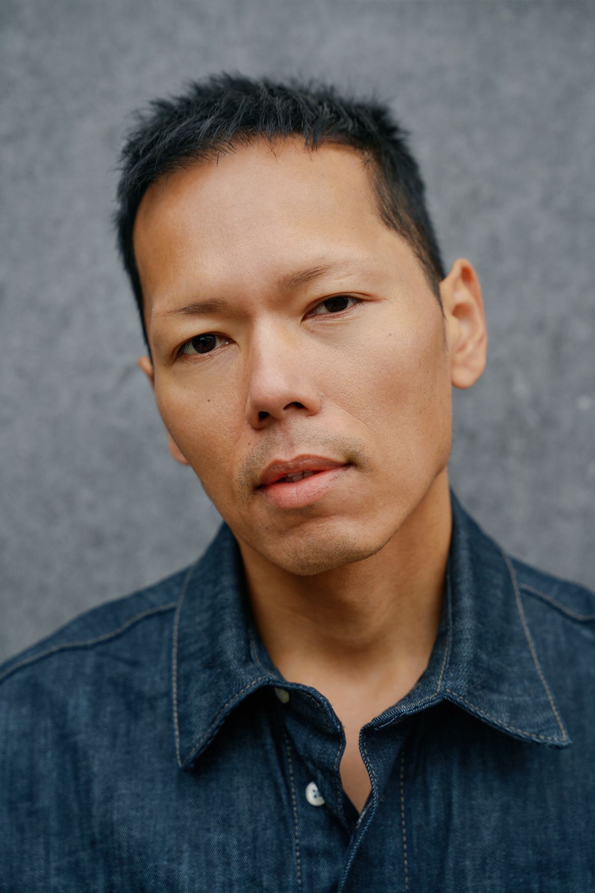 Man in donker spijkerhemd kijkt naar de kijker. Grijze achtergrond.