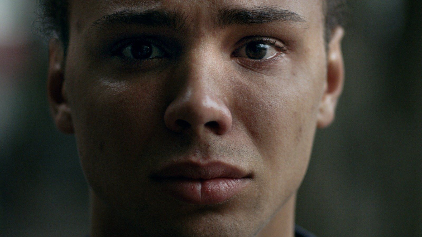 Man met bruine ogen, met tranen in zijn ogen, kijkt de kijker aan; neutrale achtergrond.