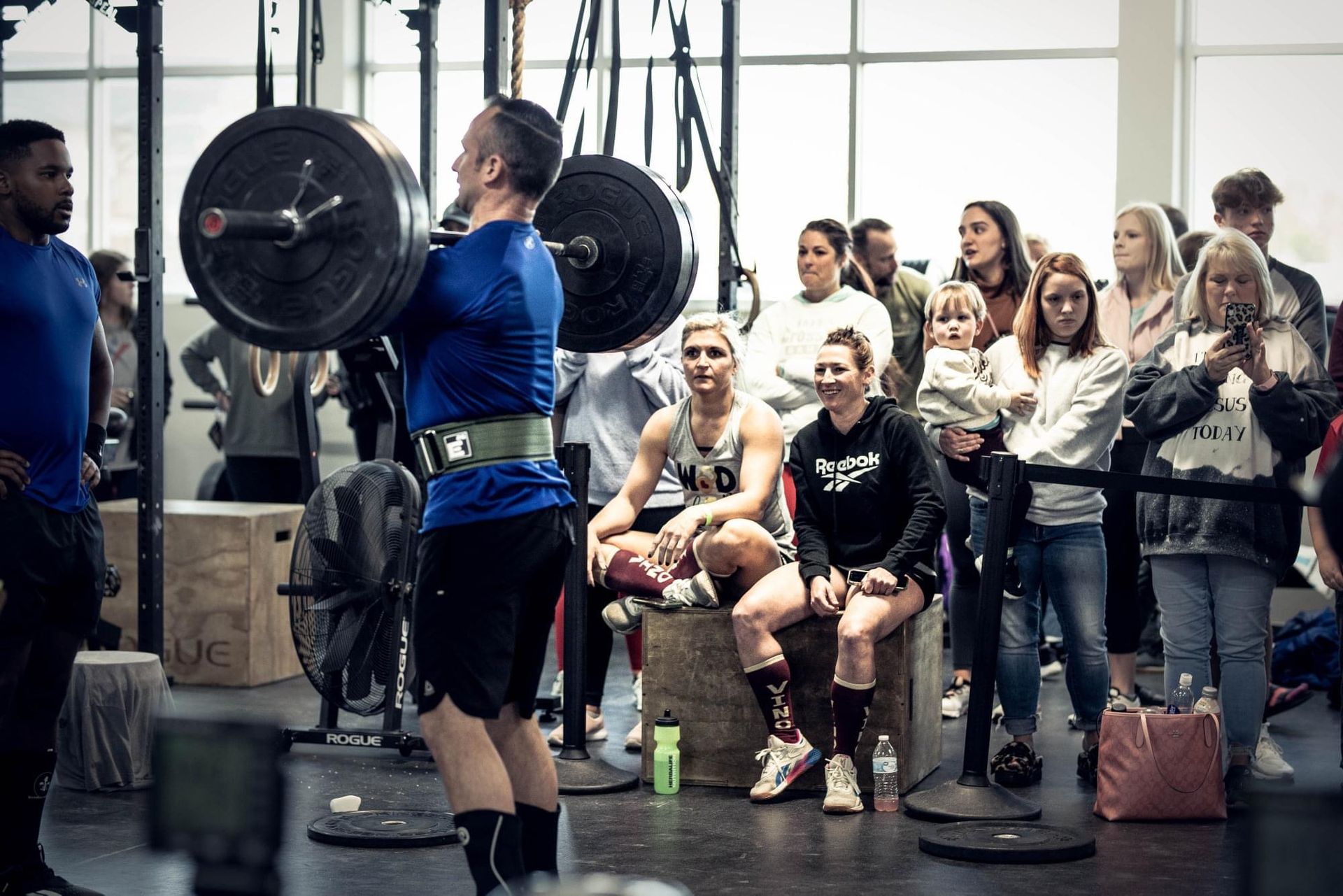 Group of people posing in a gym. Some are kneeling, wearing athletic gear. A child is kneeling.