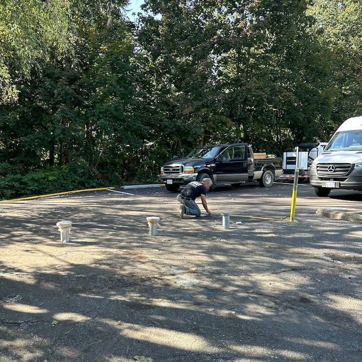 A man is kneeling down in a parking lot installing bollards