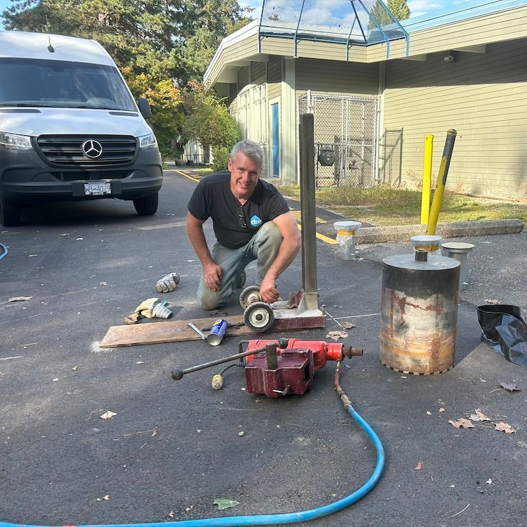 A man is kneeling down in front of a van installing bollards