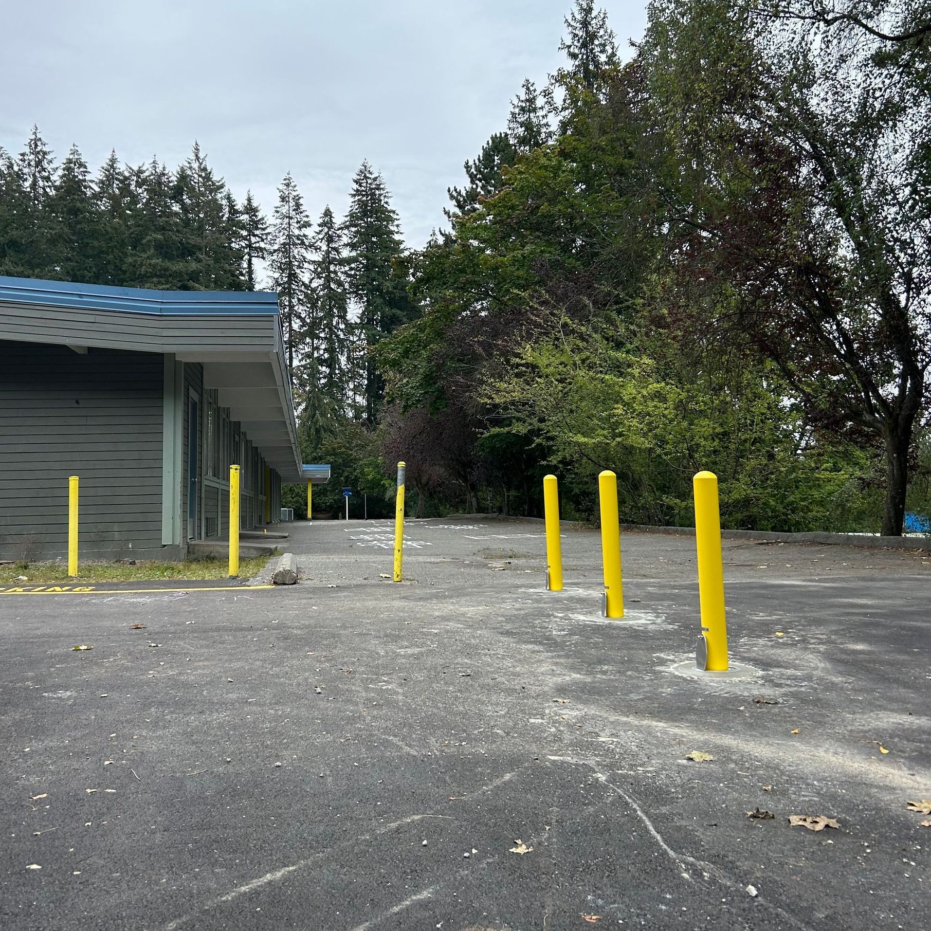 A parking lot with yellow bollards and a building in the background