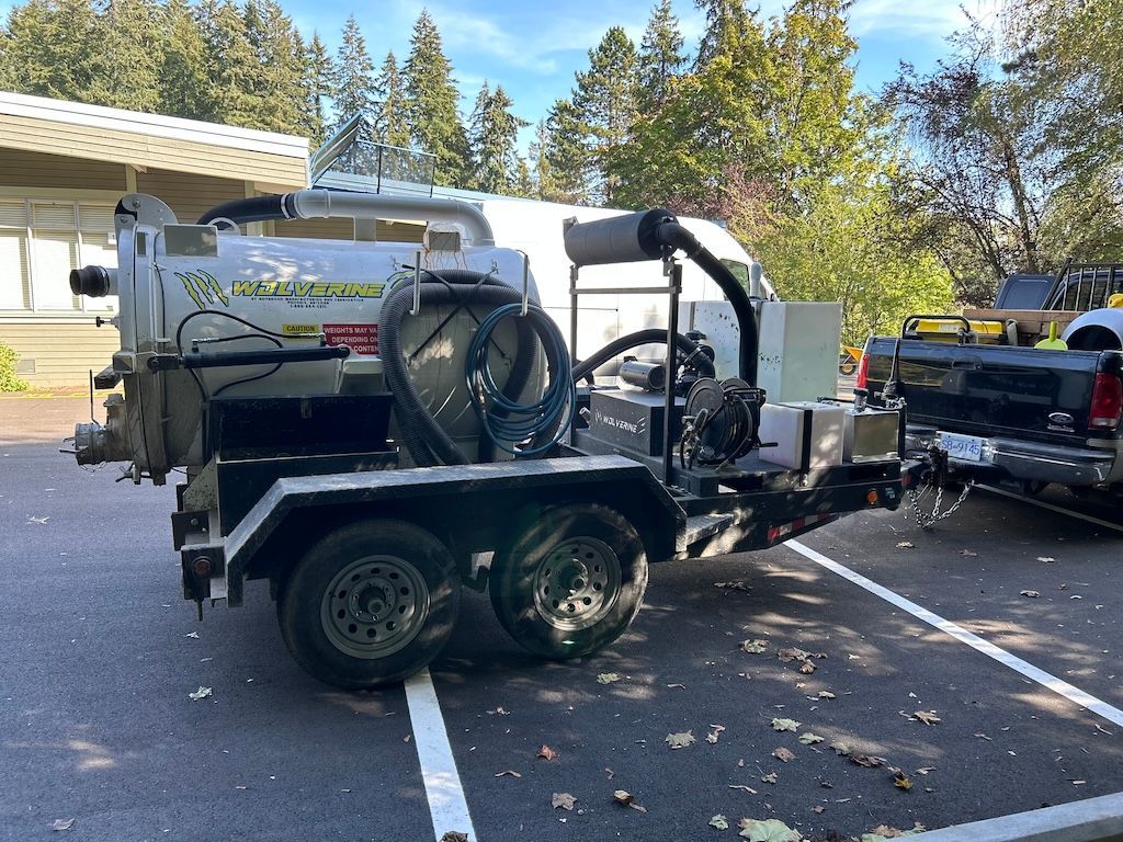 A vacuum truck is parked in a parking lot next to a truck installing bollards