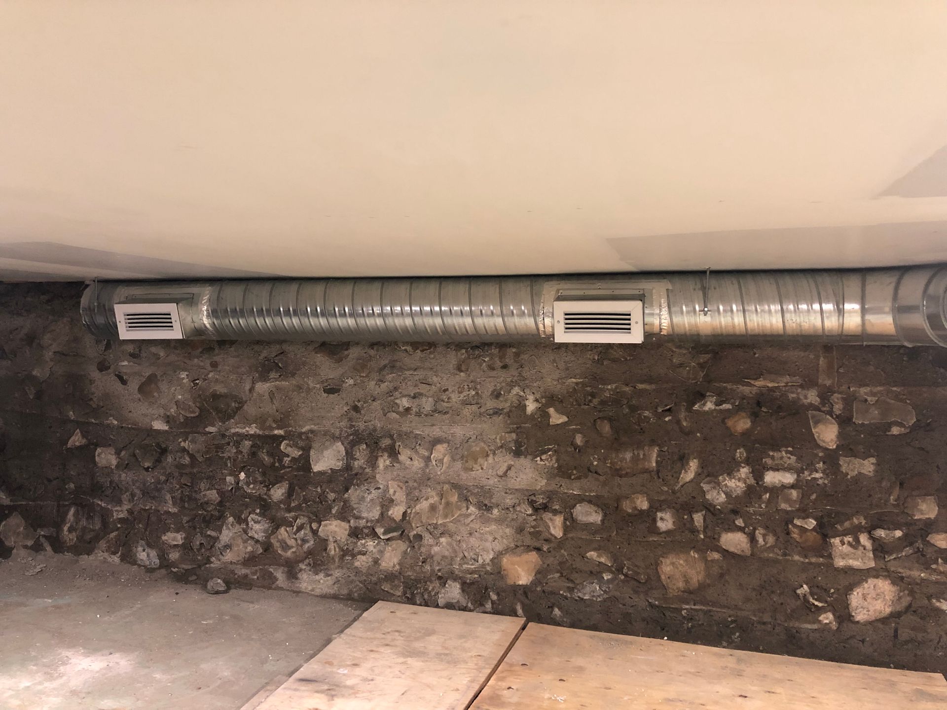 Un tuyau métallique est suspendu à un mur de briques dans un sous-sol.