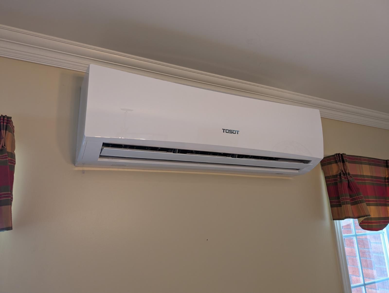 Un climatiseur blanc est accroché à un mur à côté d'une fenêtre.