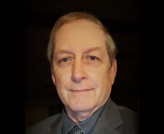 Man with light skin and gray hair wearing a suit, smiling at the camera.