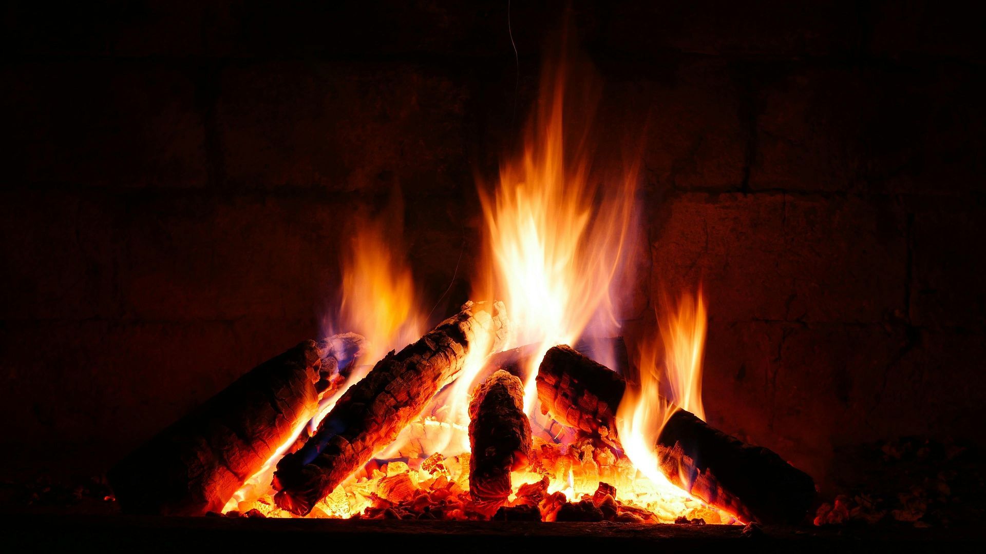 Fire burning in a fireplace: orange flames, burning logs, dark brick background.