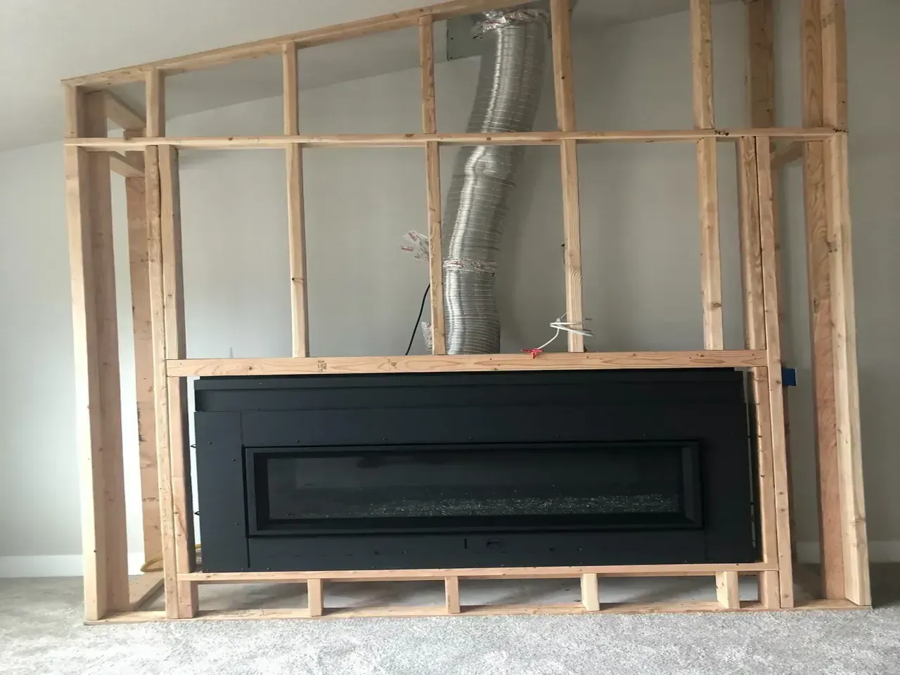 A black fireplace installed in a wood frame, with a silver vent pipe.