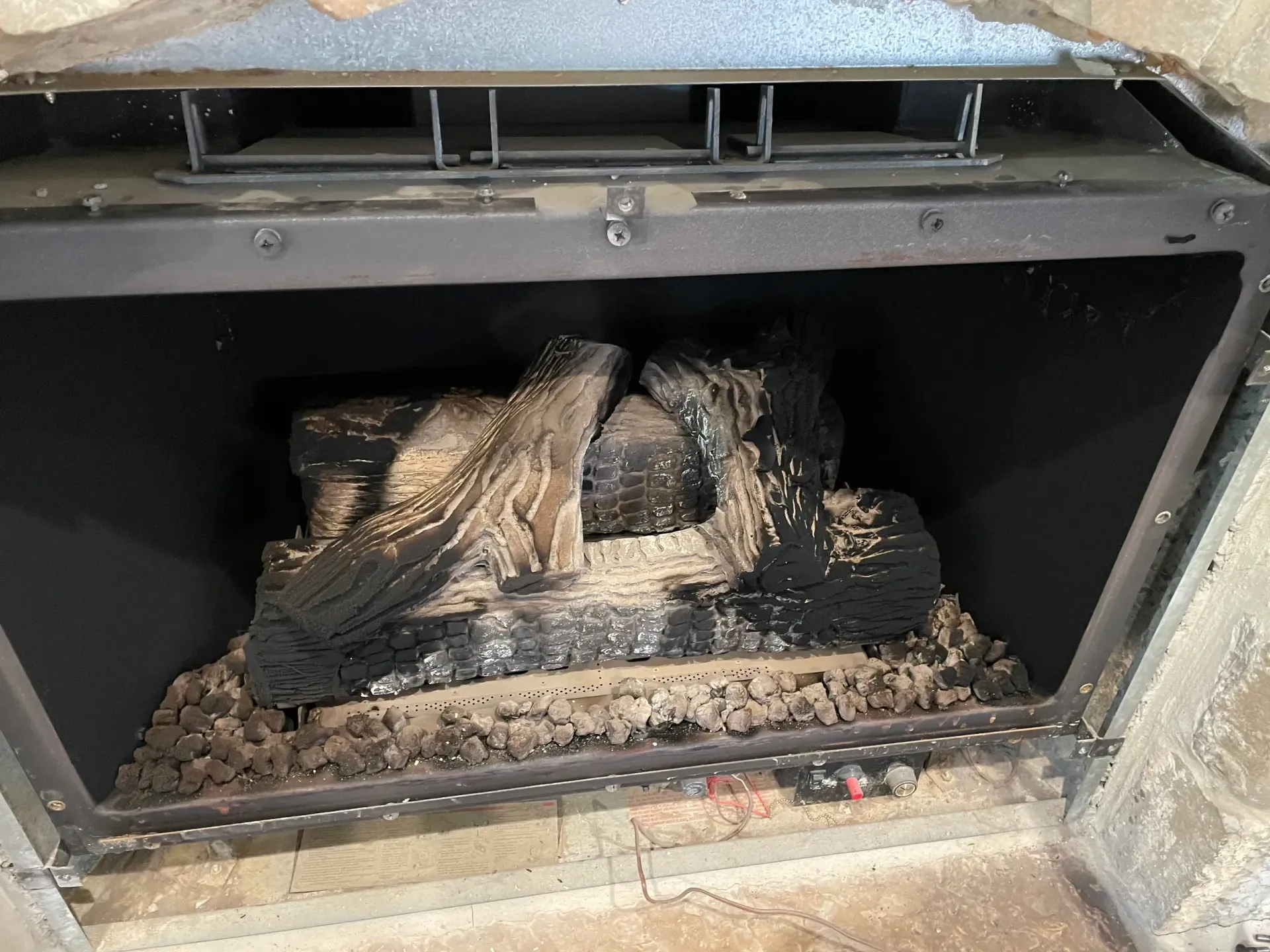 A gas fireplace interior with ceramic logs covered in soot.