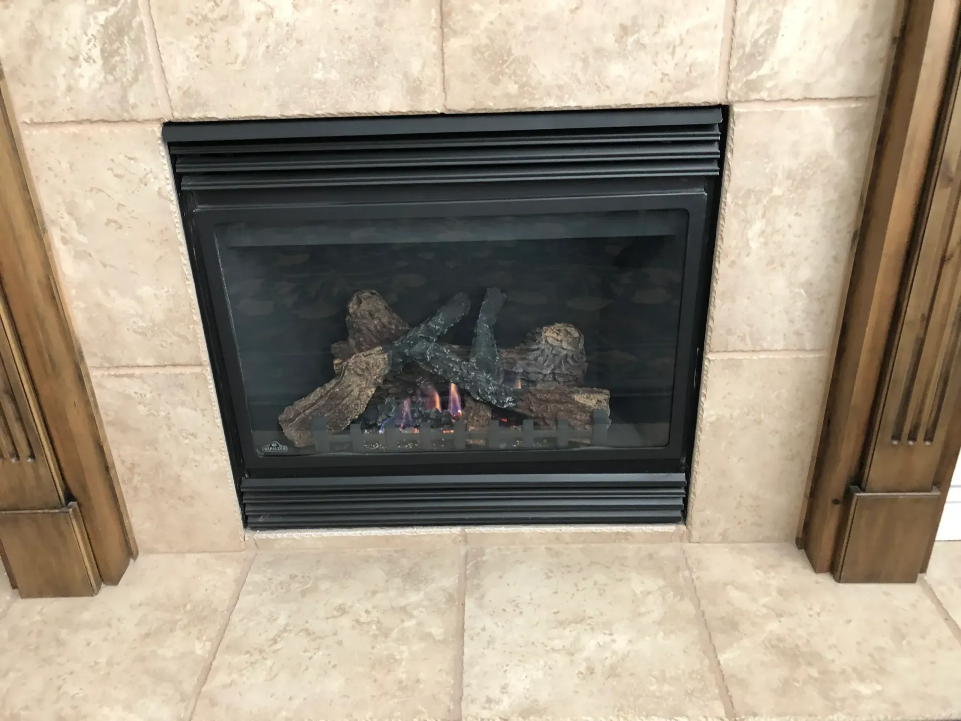 Black gas fireplace with faux logs burning, set in a beige tiled surround.