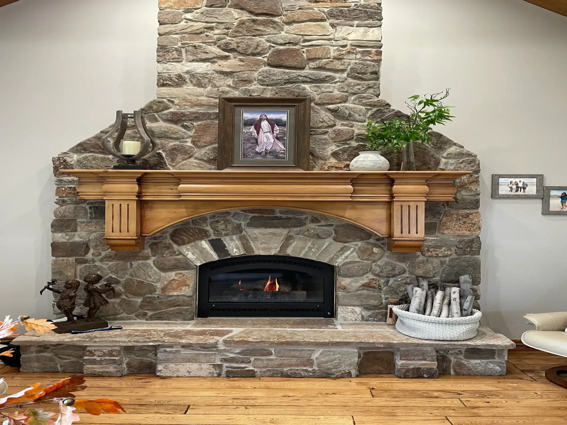 Stone fireplace with wooden mantel, a framed photo, and a burning fire.