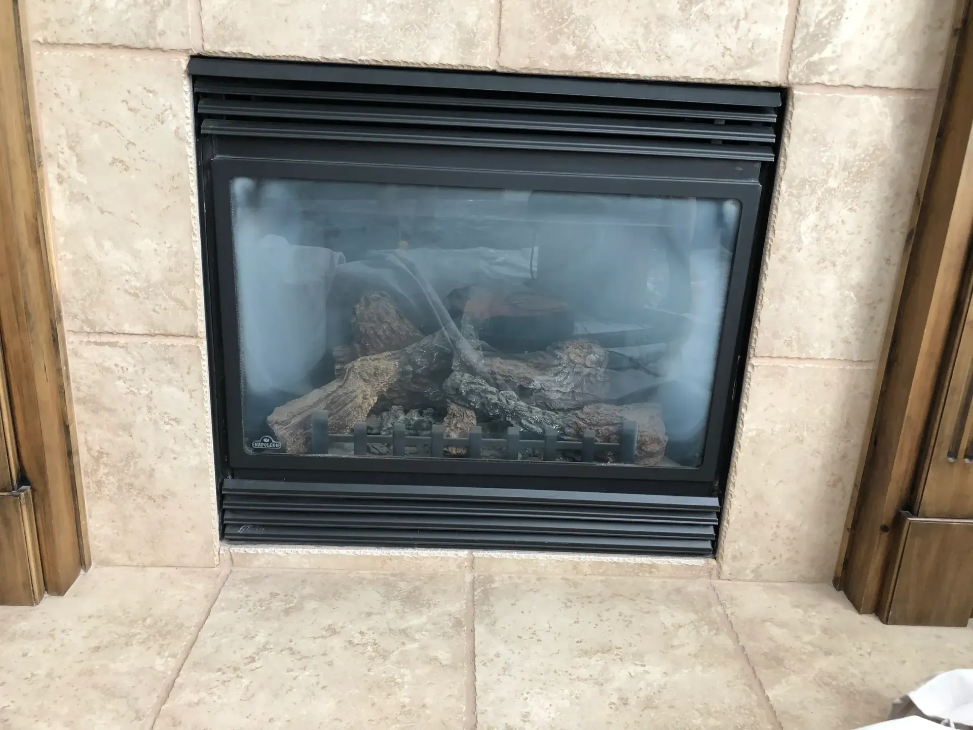 Gas fireplace with black frame, tan tile surround, and artificial logs inside.