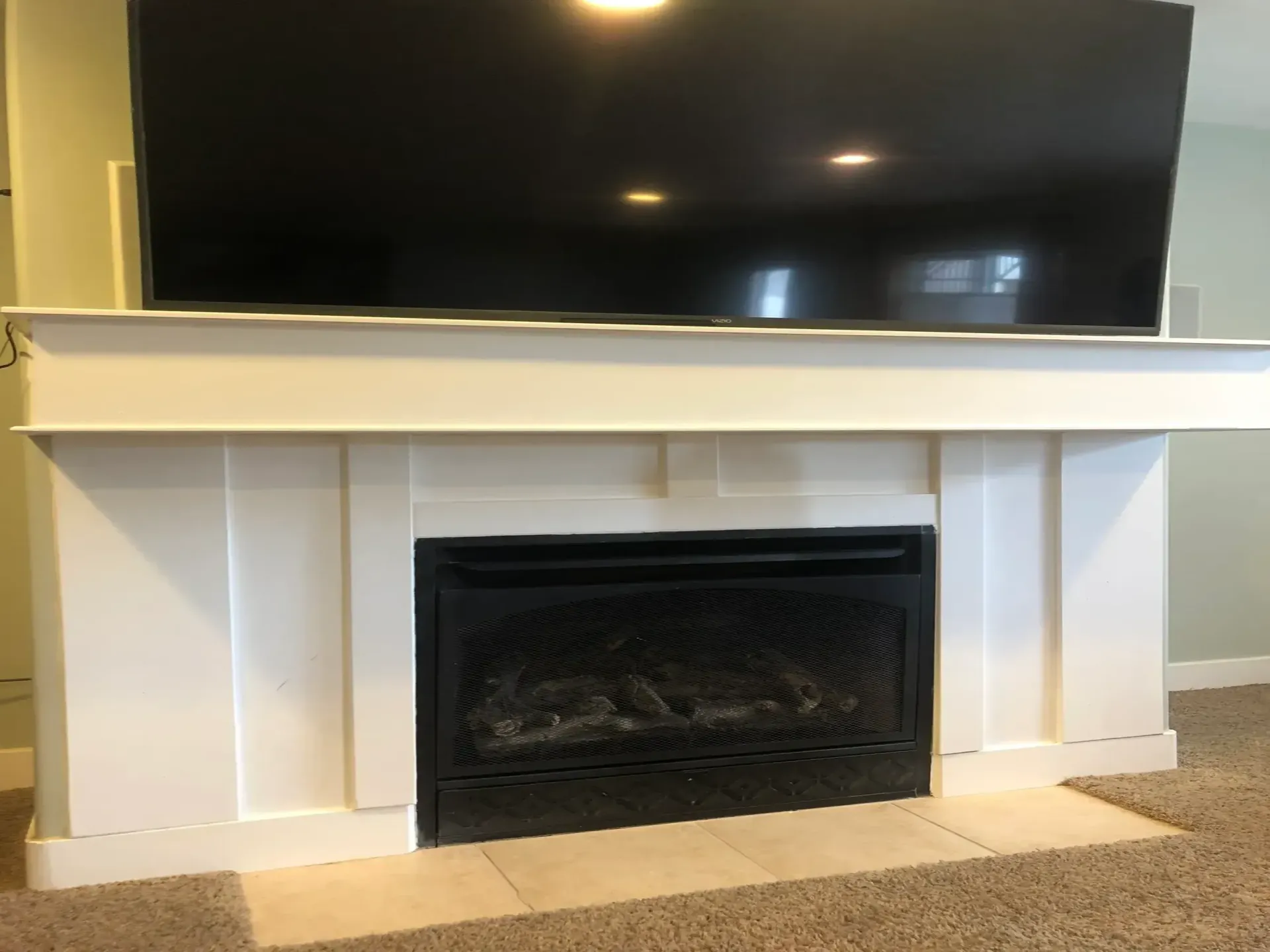 White fireplace with black firebox, beige hearth, and large TV mounted above.