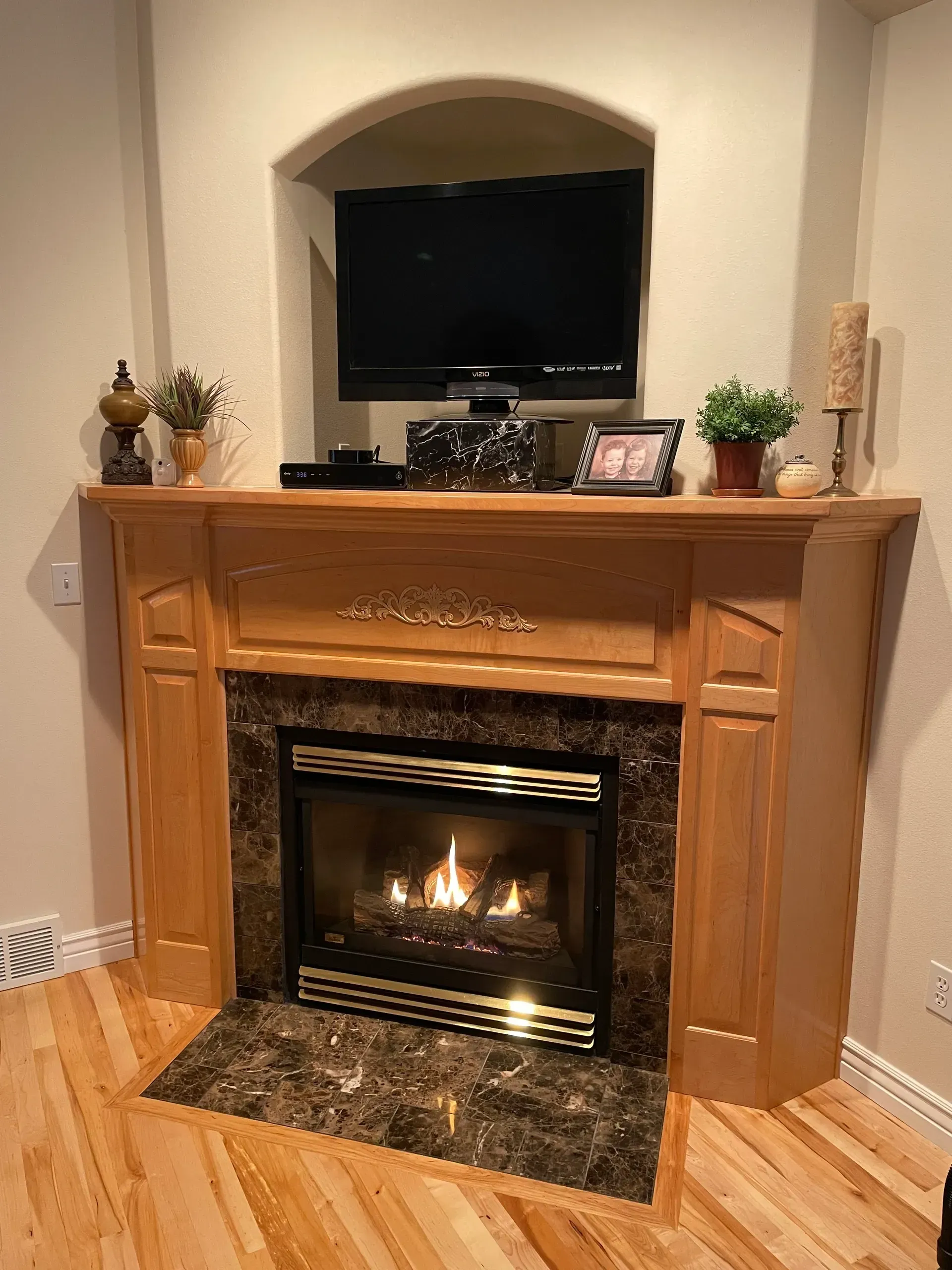 A gas fireplace with a wood mantel, TV above, and decorative items.