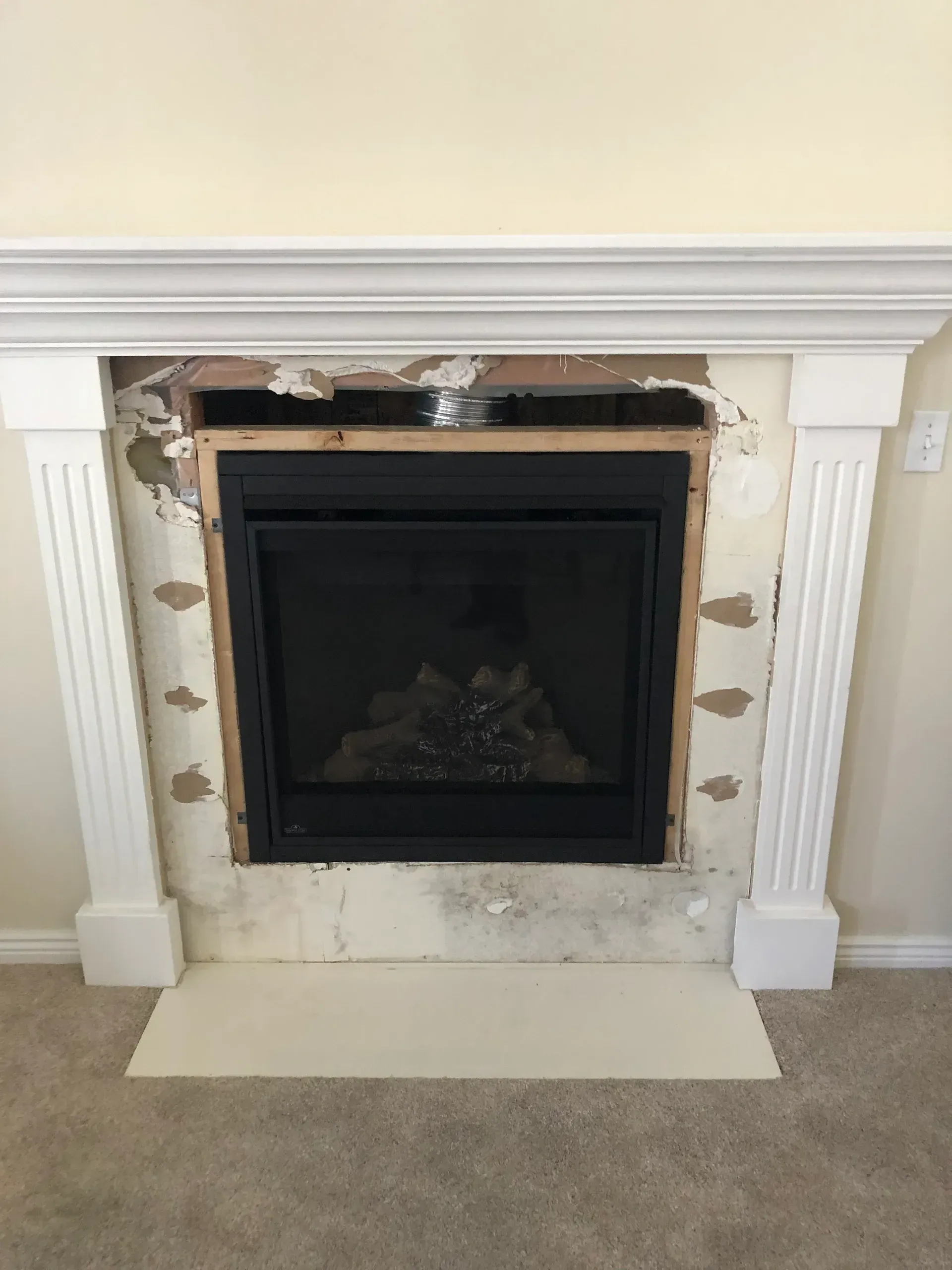 Fireplace with damaged surround, missing drywall, and white mantel. Black firebox is centered.