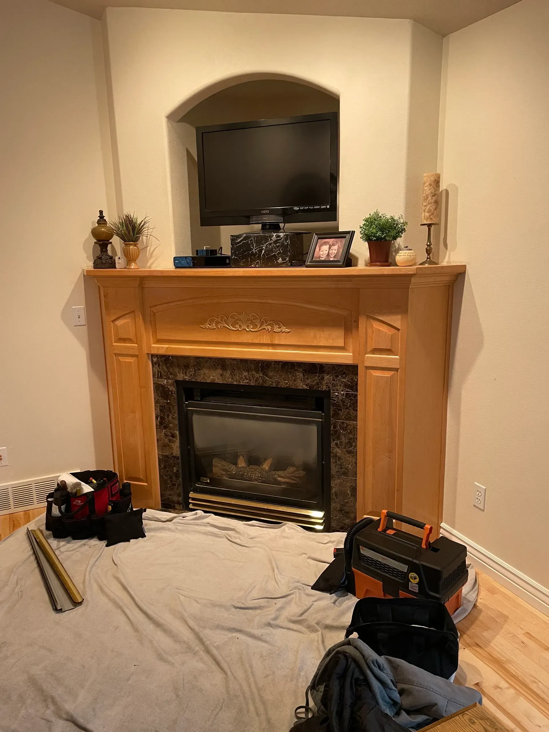 Wooden fireplace with an electric fire, a TV above, and tools on a drop cloth.