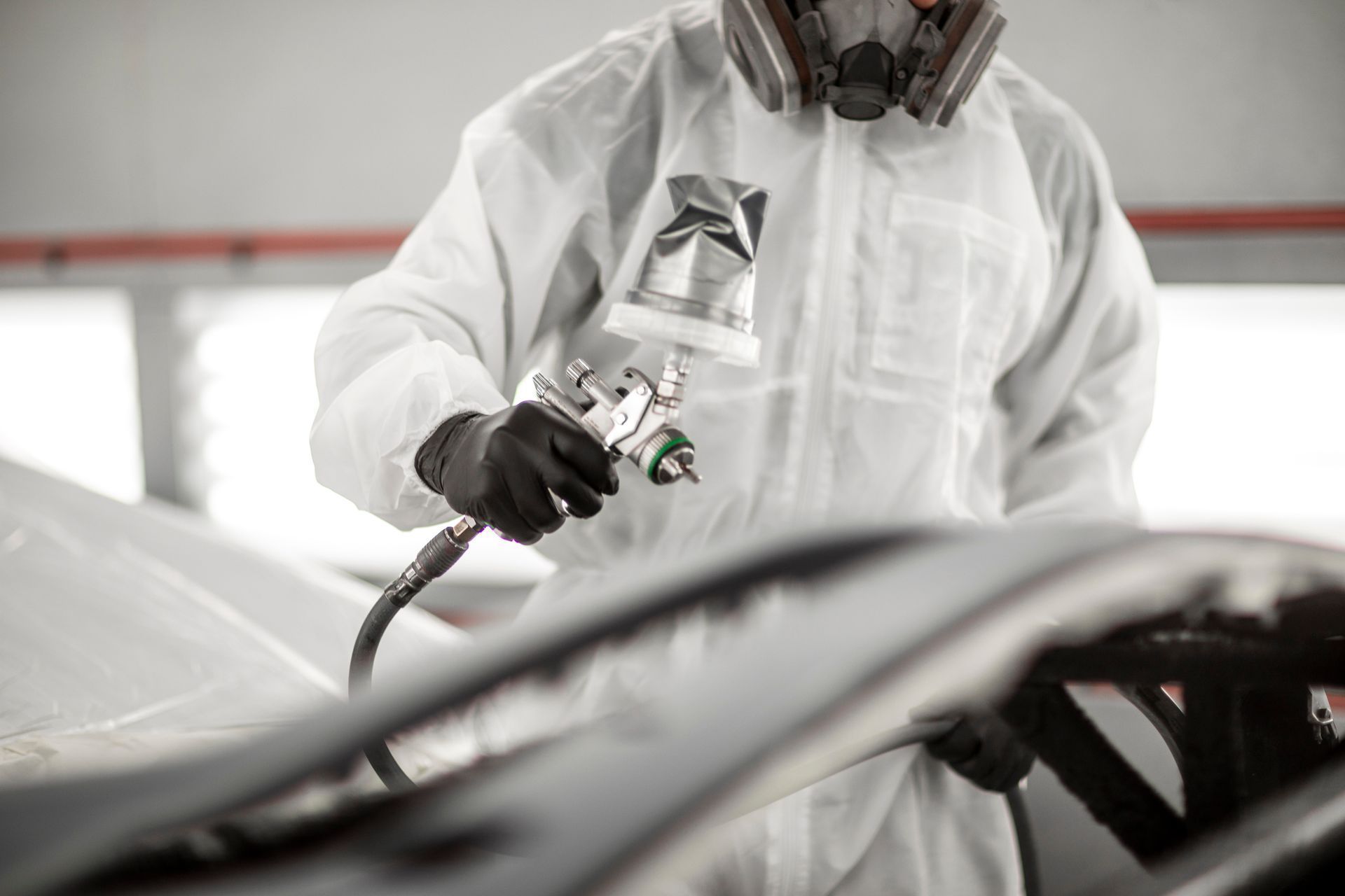 Worker in a white protective suit spraying paint on a car body in a workshop