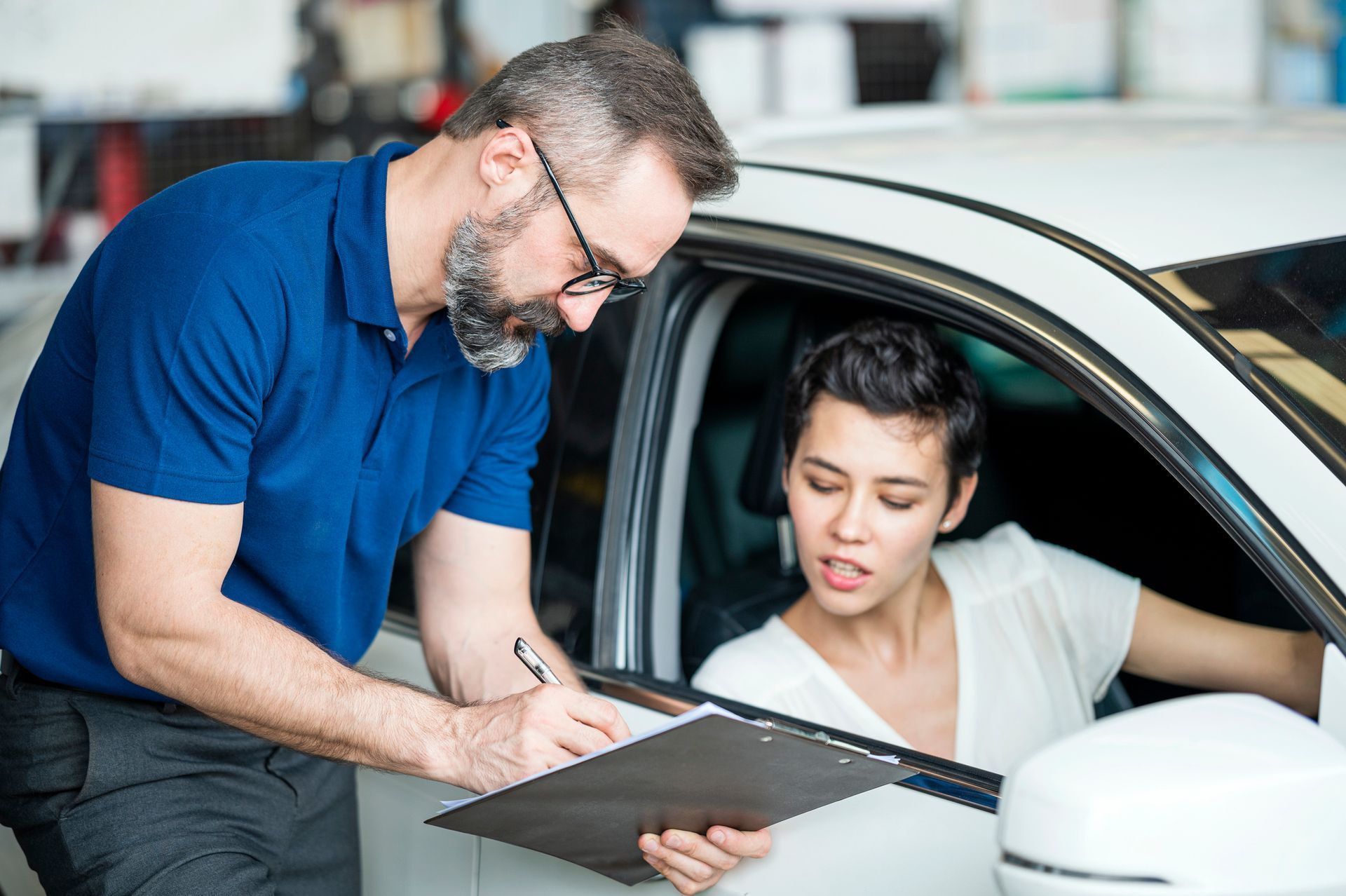 Mechanic explaining a repair estimate to a customer beside a white car