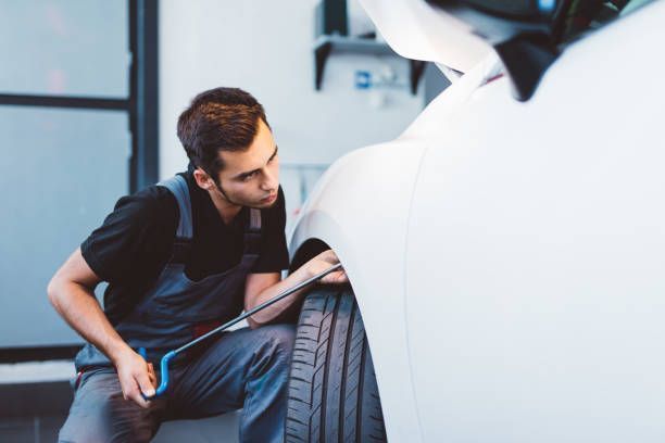 Mechanic inspecting a car tire under the raised hood in a garage