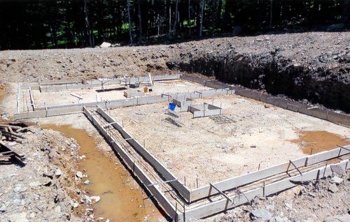 Concrete foundation forms on a construction site, with dirt and surrounding trees.