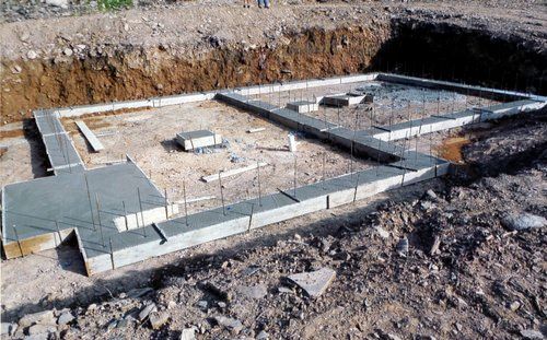 Concrete foundation under construction, set in a trench, with rebar visible.
