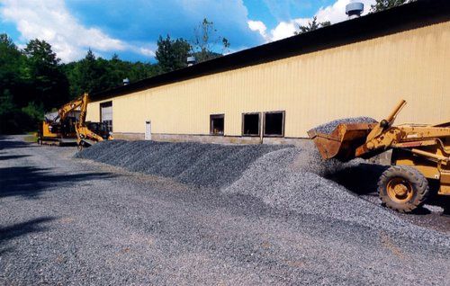 Construction site: yellow building, two tractors moving gravel; bright, sunny day.