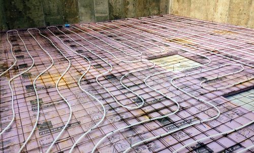 Pipes for radiant floor heating laid on insulation and rebar mesh, ready for concrete pouring.