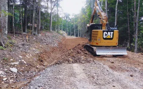 Yellow CAT excavator constructing a dirt road through a forest.