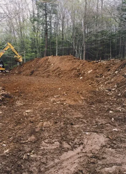 Dirt clearing in a forest with an excavator and a large pile of earth.