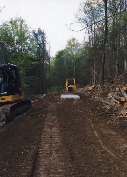 Dirt path being cleared by construction vehicles in a wooded area.