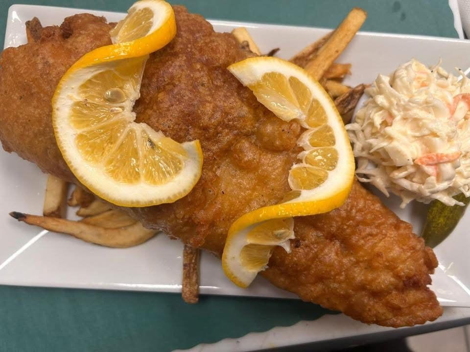 A plate of fish and chips with lemon slices and coleslaw