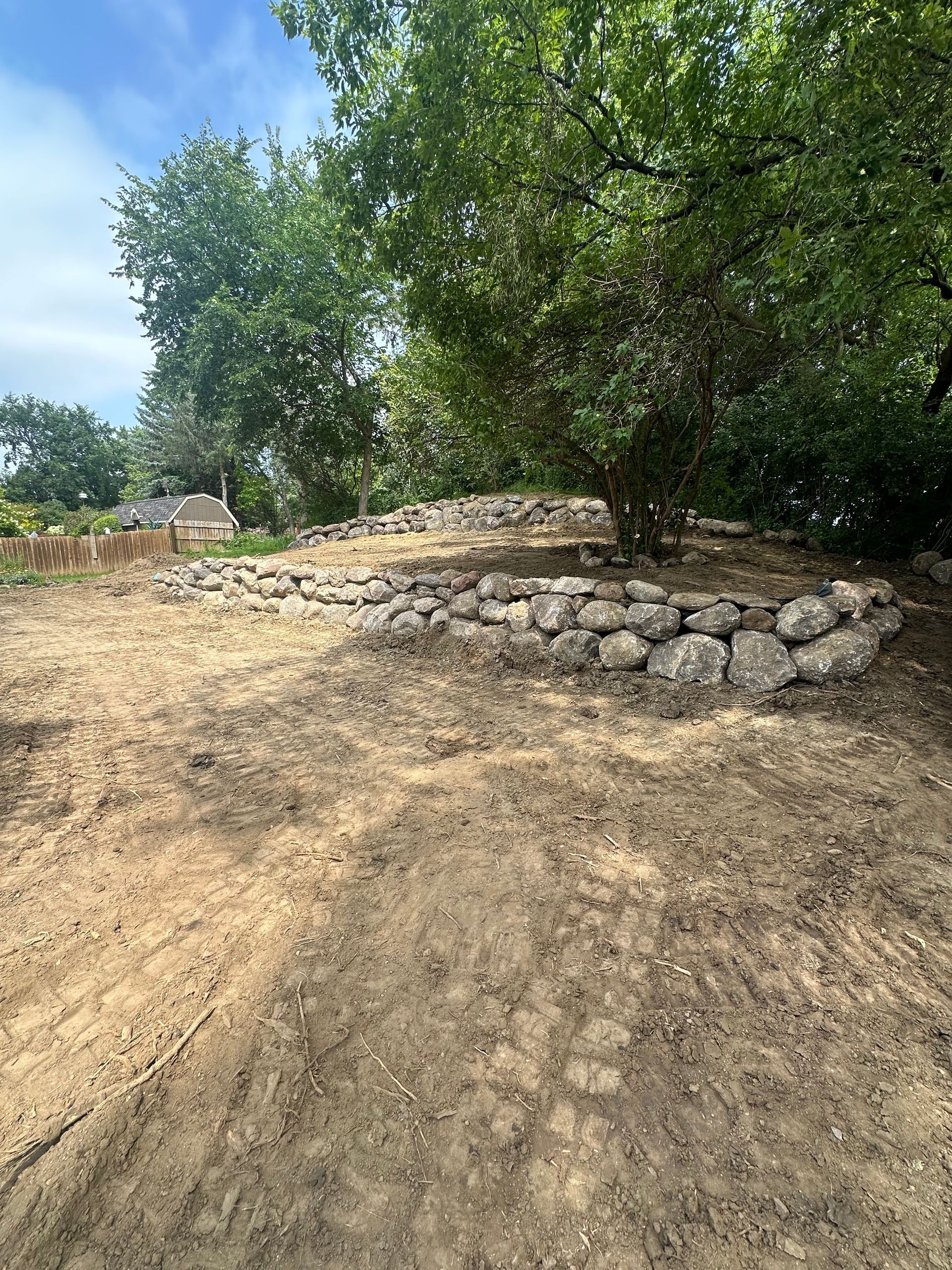 A pile of rocks in the middle of a dirt field with trees in the background.