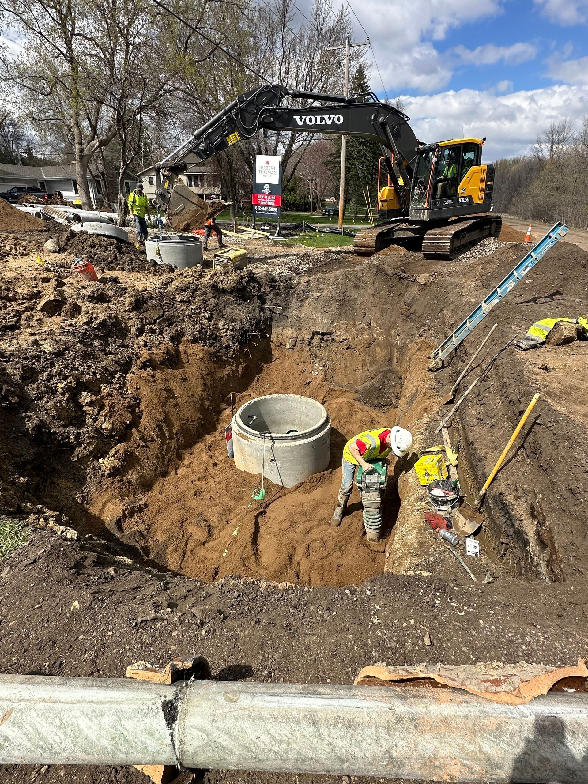 A man is digging a hole in the dirt next to a large excavator.