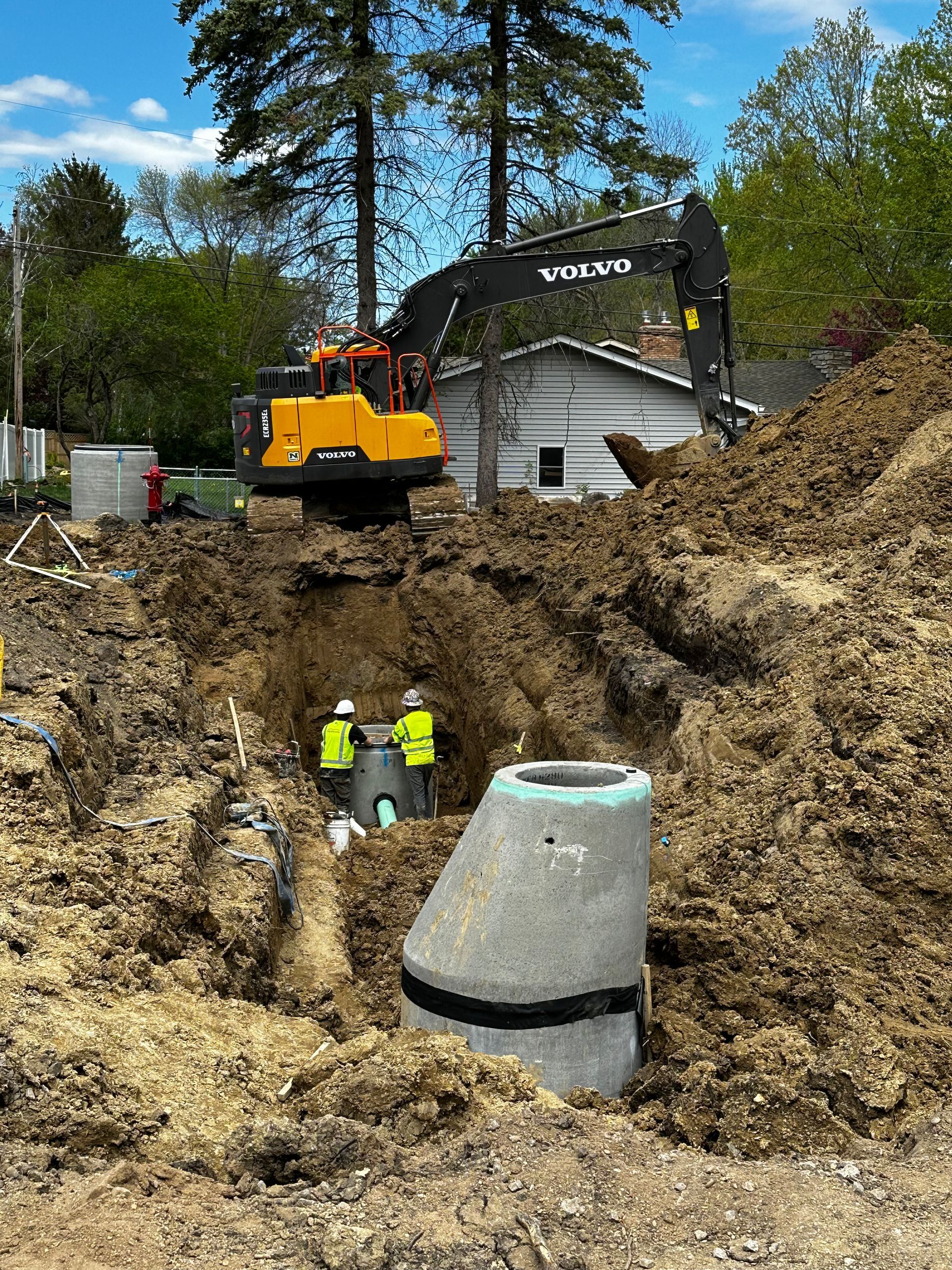 A yellow excavator is digging a hole in the dirt in front of a house.