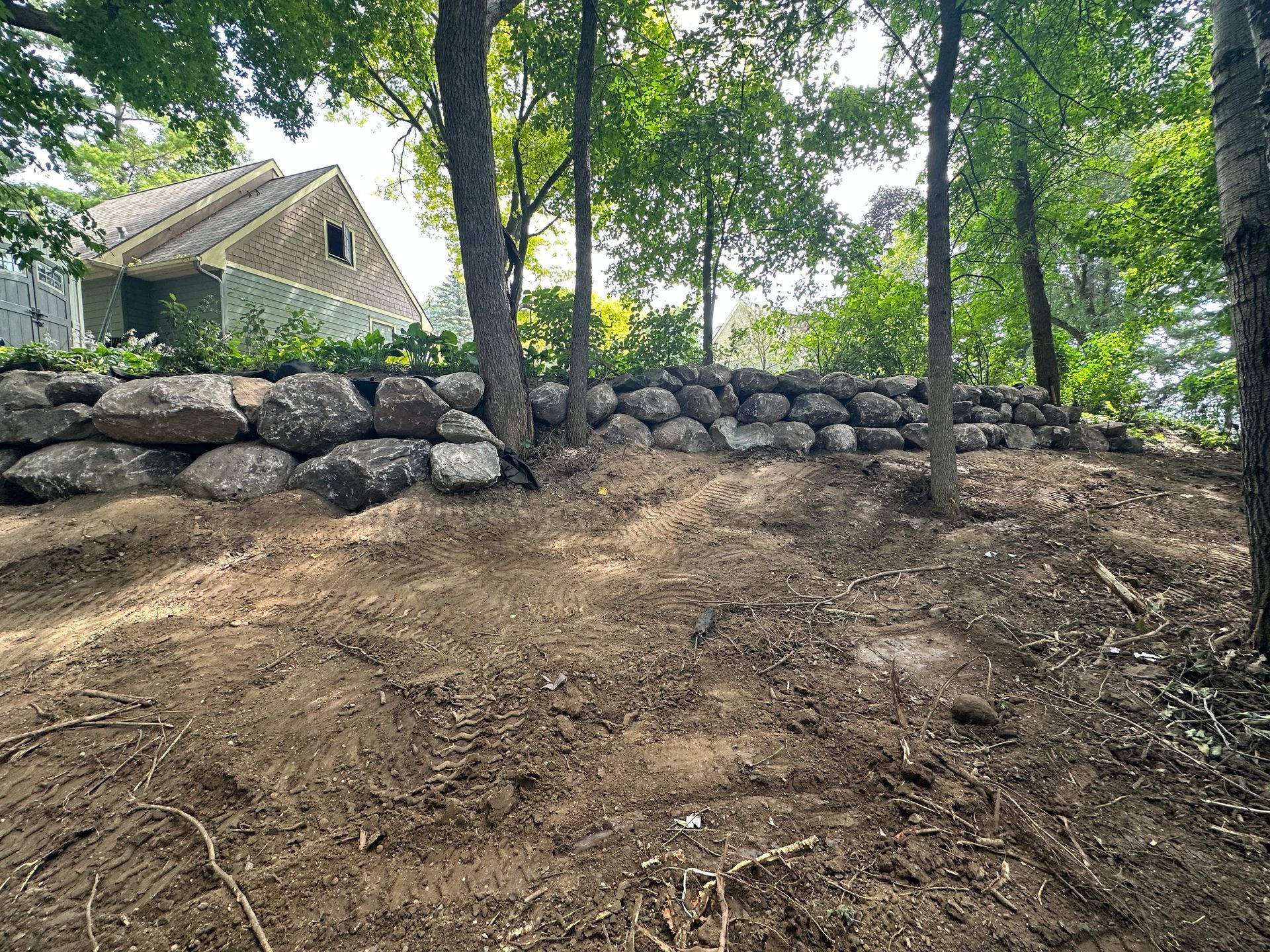A large rock wall is sitting on top of a dirt hill in the middle of a forest.