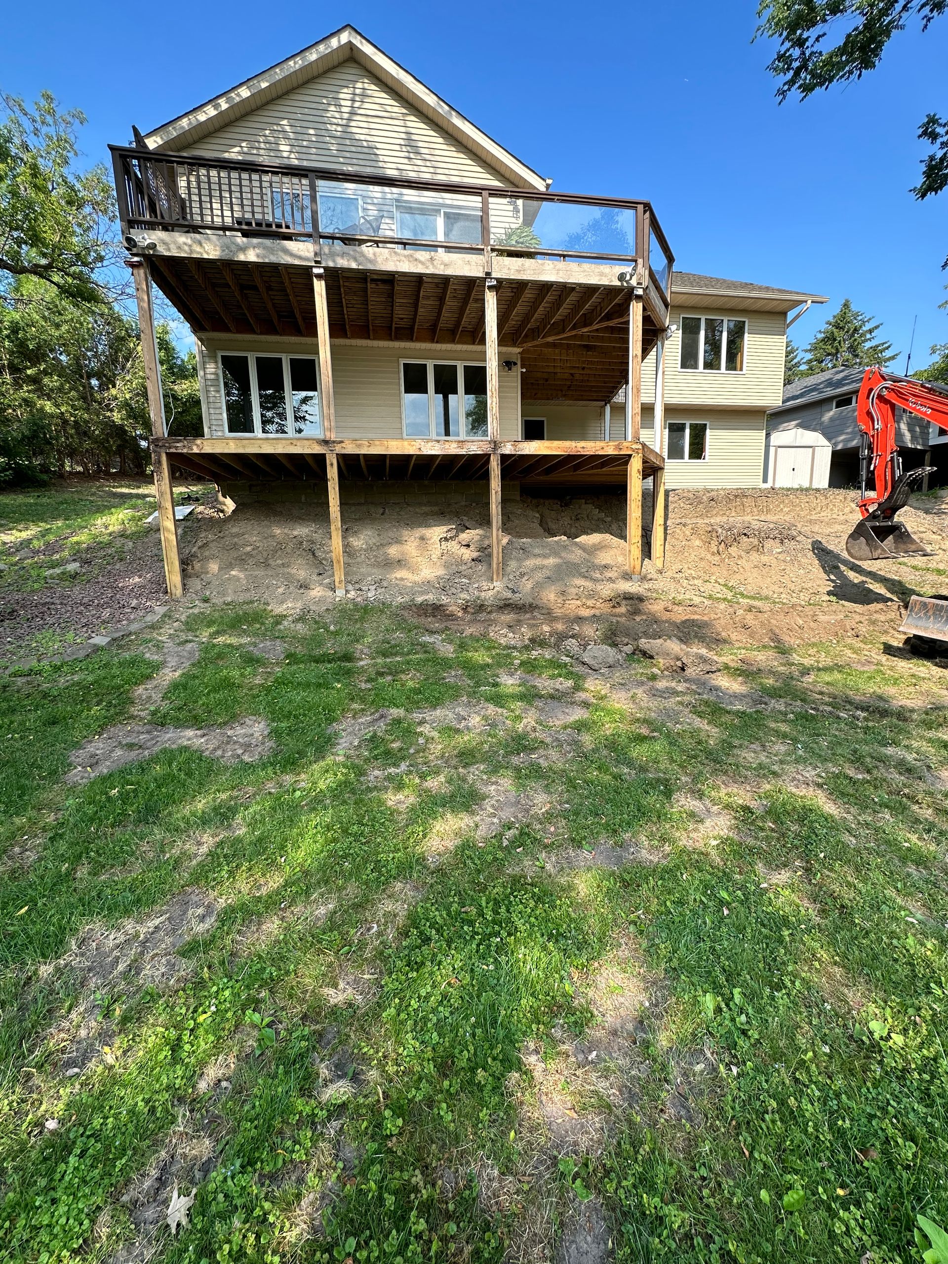 A house with a large deck is sitting on top of a grassy hill.