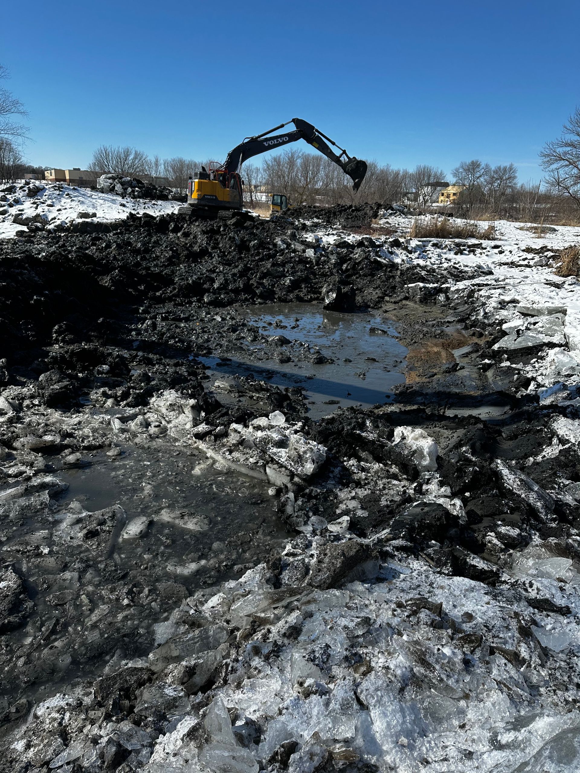 A large excavator is digging a hole in the snow.