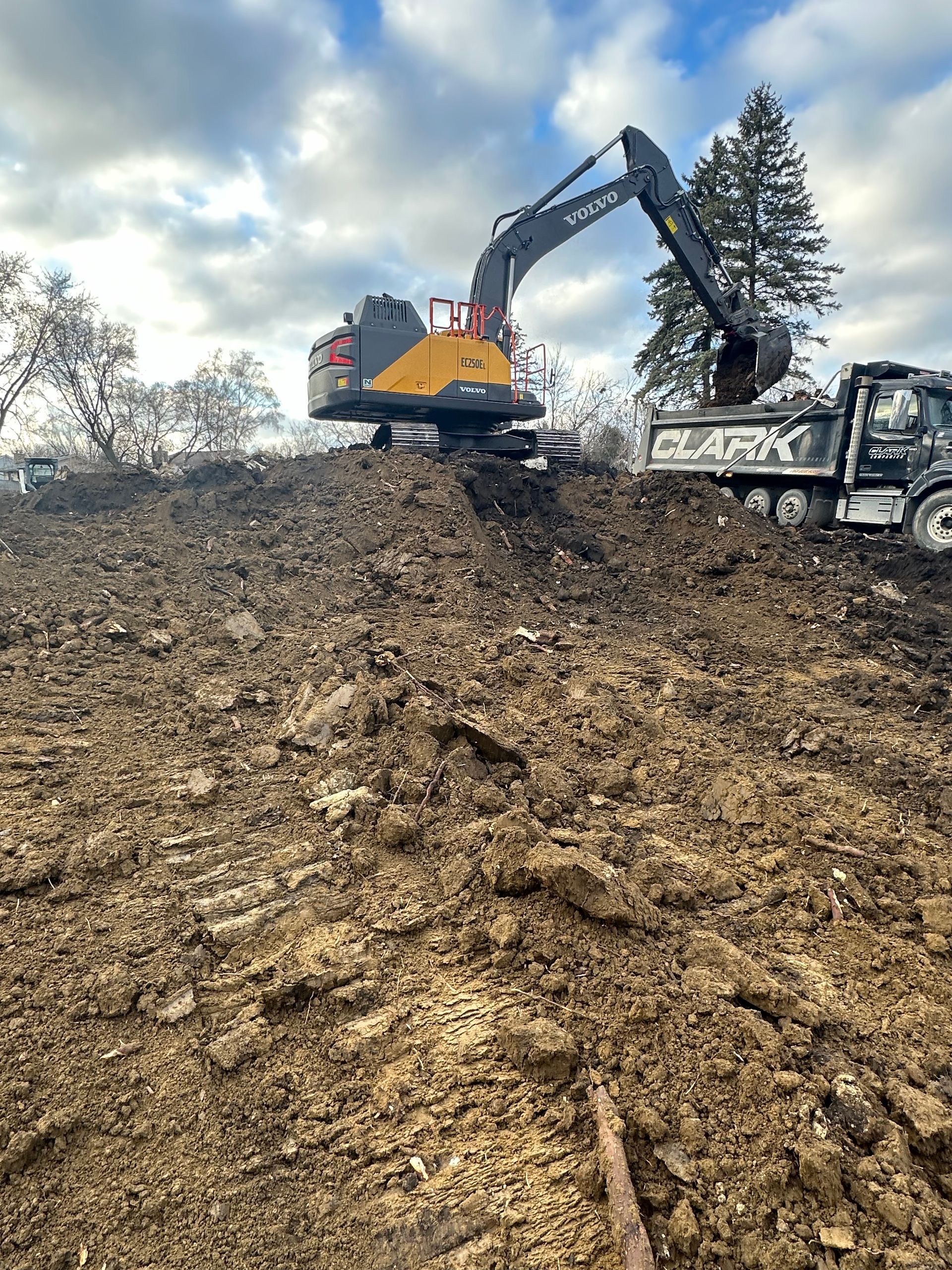 A large excavator is digging in a pile of dirt next to a dump truck.