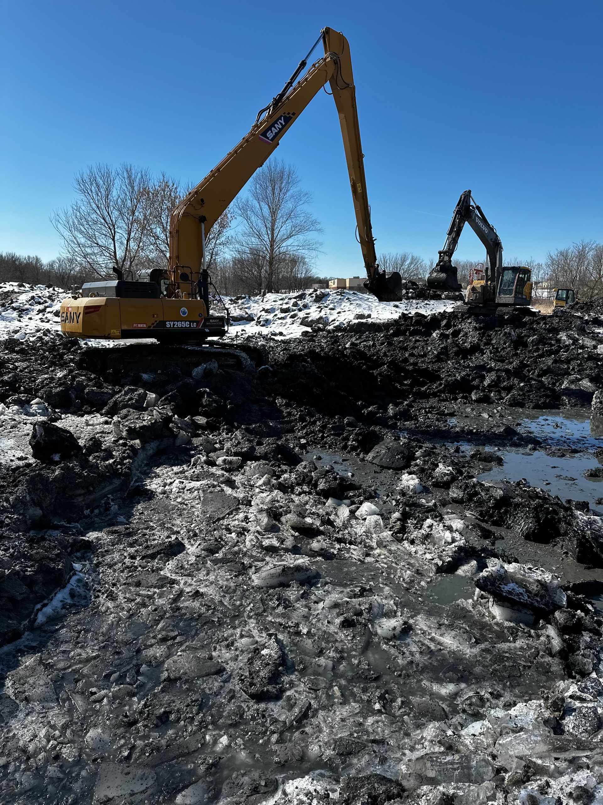 Two excavators are working in a muddy field.